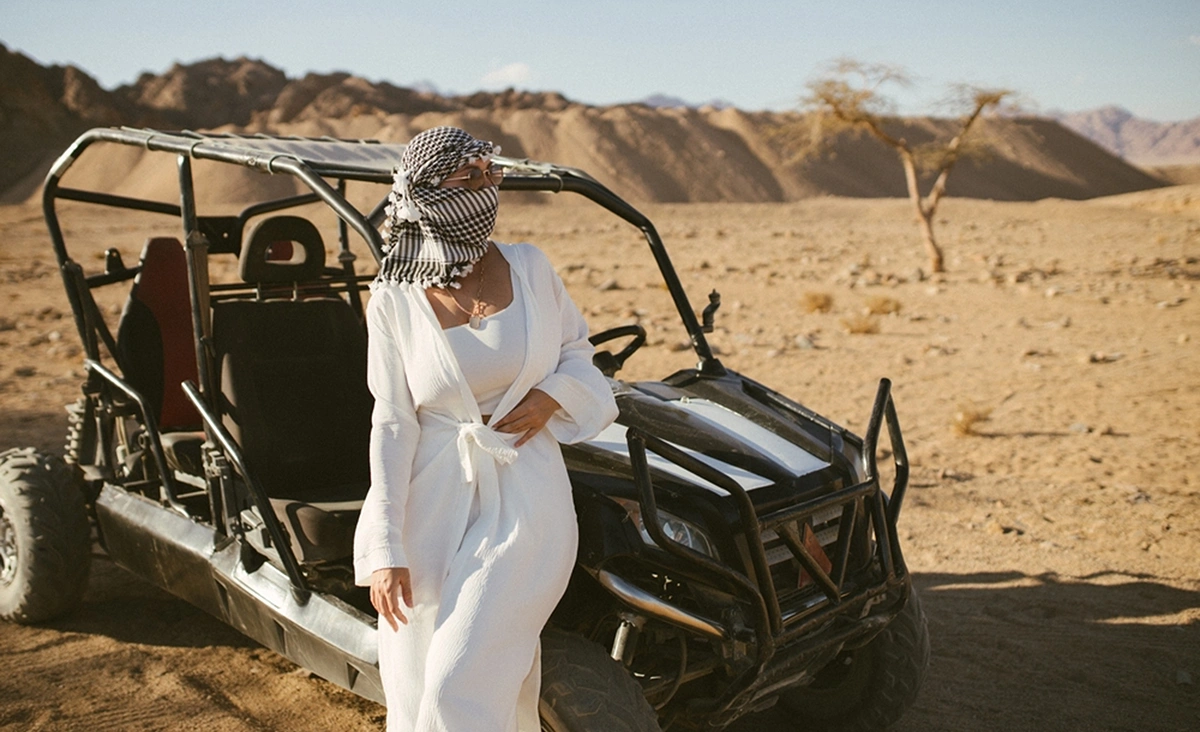 Femeie in alb langa un jeep in timpul unui safari in desert