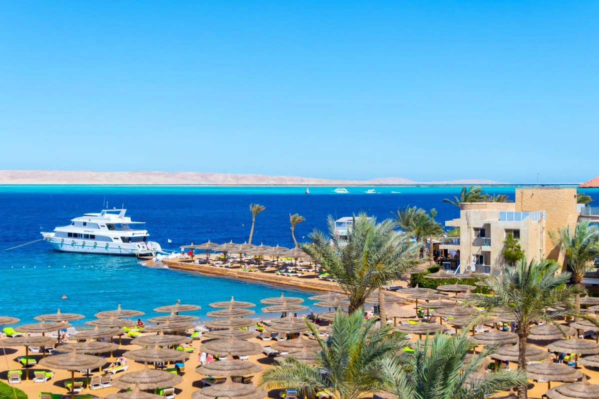 plaja in Hurghada intr-o zi senina, cu umbrelute, palmieri, vapor in departare