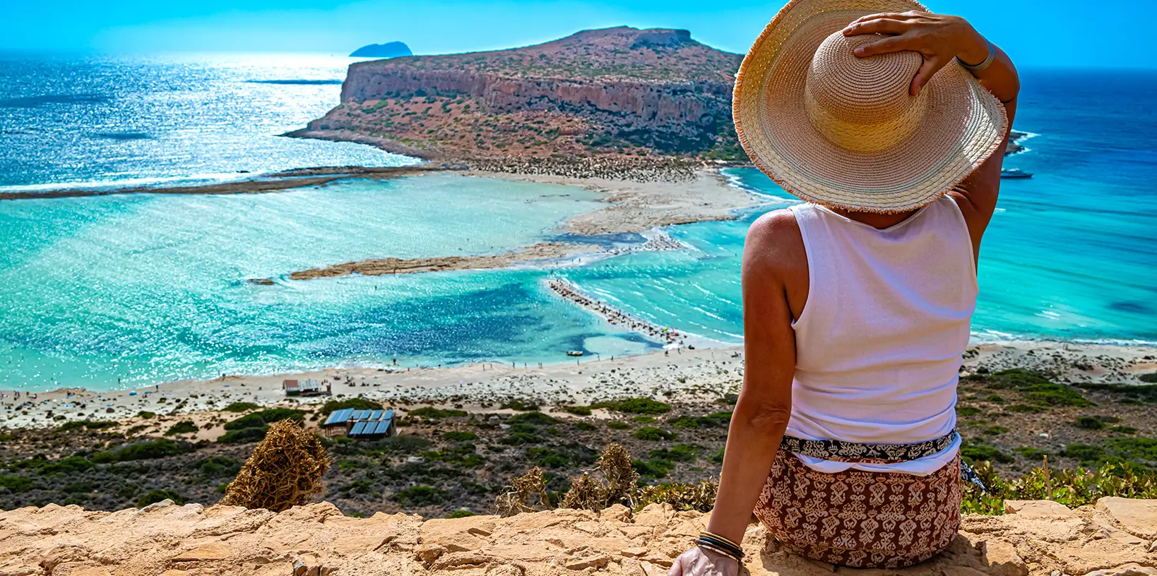 turista cu maiou alb si palarie de plaja admirand peisajul din insula creta
