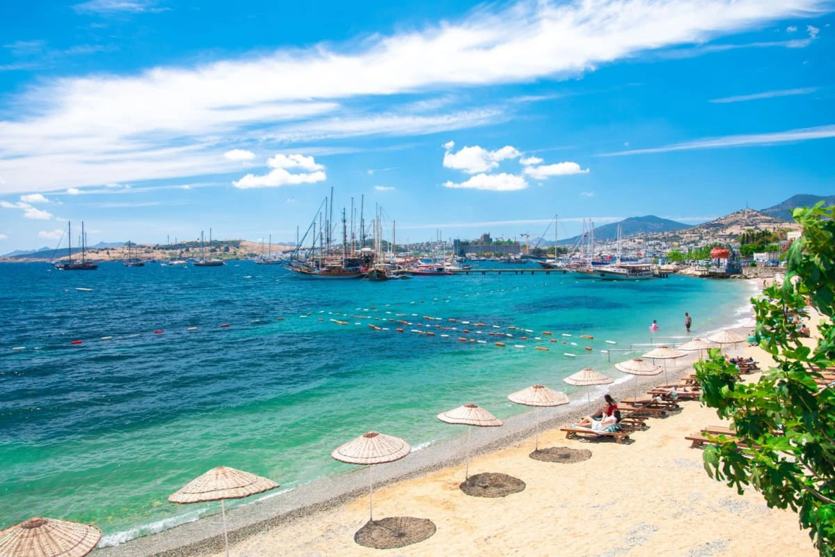 plaja Bodrum, cu umbrelute pe nisip, iar pe fundal sunt iahturi pe mare